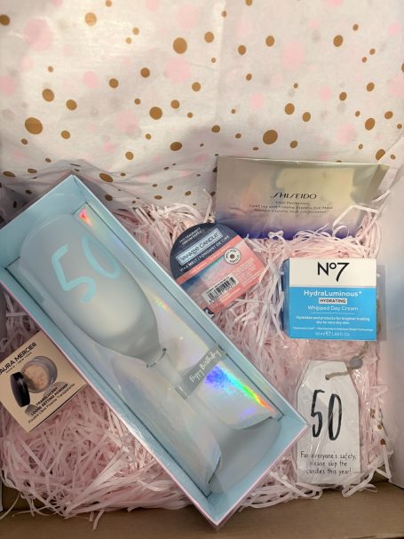 50th gift set for a customers friend - the remit was "she loves No7, candles and chocolate". A gift box containing a celebratory glass, skincare products, and decorative paper.