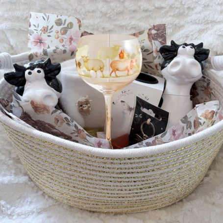 A gift basket for a lady who loves cows and had recently suffered a loss - from her Cousin to let her know she was thinking of her. A basket containing cow-shaped decorations, a glass, and floral-patterned items.